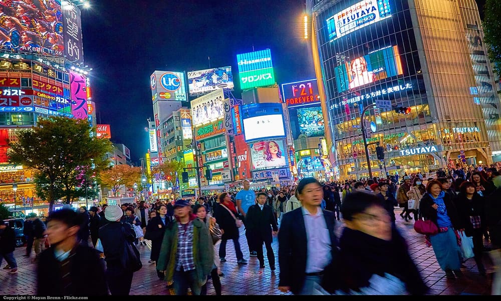 A crowd crossing beneath advertising screens in Shibuya at night